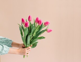 bouquet of pink tulips in children’s hands on beige background . Spring Backdrop greeting for Mother’s Day .  Pantone 2024 peach fuzz background 