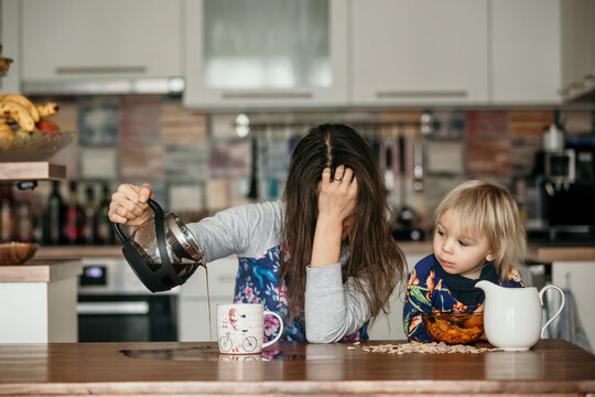 Tired Mother, Trying To Pour Coffee In The Morning. Woman Lying On Kitchen Table After Sleepless Night