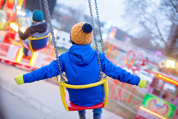 Child, cute boy riding chain swing carousel on sunset, motion blur