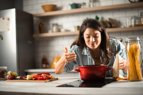 Beautiful pregnant woman preparing delicious food. Smiling woman cooking pasta at home