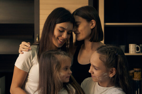 Staged Photo. Lesbian Couple And Their Children In The Kitchen. The Kids Are The Main Chefs. We Can Paint With Flour! Everyone Is Covered In Flour, But No One Is Angry.