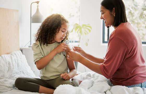 Loving mother comforting her daughter with a bandaid in bed, being affectionate and caring at home. Young parent helping her sick child, applying a plaster and bonding, special moments of motherhood