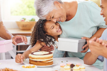 Hug, happy and gift giving of a grandmother and girl with birthday cake at a party celebration. Happiness of people at a children event to celebrate with food, family and friends smile at a home