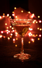 Clear glass of martini with olives , focus on a olives on a night club setting, and blurred background light
