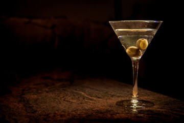 A clear glass of martini, focus on olives on a night club marble bar counter 