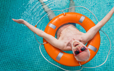 Happy senior man swimming with lifesaver and relaxing in the swimming pool