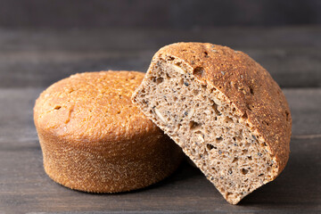 Two round sourdough loaves of bread with one sliced loaf with seeds on dark wooden background, closeup image