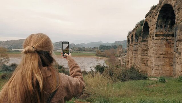 Woman travel blogger vlogger taking photo antique ruins arch building social media content