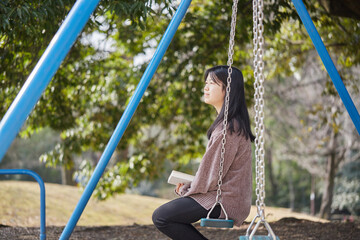 春の公園のブランコに座って読書している女子中学生の姿