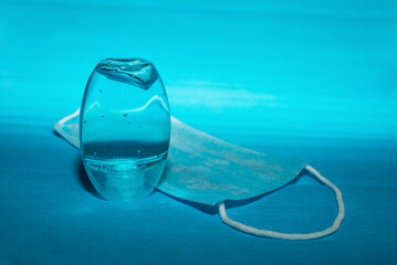 Plastic bottle of the blue pocket antiseptic gel and a protective medical mask over the blue background 