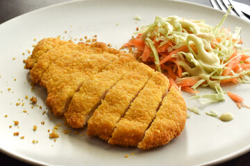 Breaded chicken schnitzel with vegetable salad included carrot and cabbage on a plate. Golden crispy fried chicken. German food.
