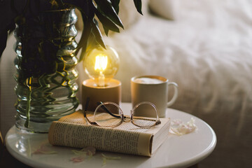 Still life details in home interior of living room. Open book with glasses, cup coffee and bouquet white pink peonies flowers. Read and rest. Cozy home