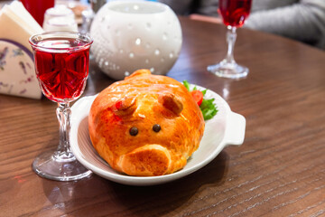 Pig shaped meat pie and a glass of cranberry tincture are on a table