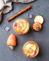 Brazilian cashew caipirinha in glasses with ice and fruit slices over stone background with copy space