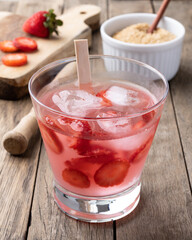 Brazilian strawberry caipirinha in a glass with ice and fruits over wooden table