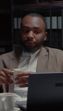 Vertical video: African american criminologists conducting investigation with research files in private detective office. Law eneforcement agents studying crime case on laptop, surveillance photos.