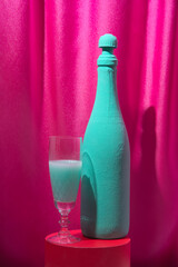 Turquoise champagne wine bottle with crystal glass on red the podium. Magenta curtains background