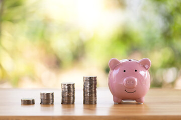 pink piggy bank smiling and coins on the table with nature blurred background, for saving money...