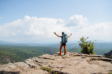guy hiker standing on the edge of a cliff keeping his hands to the sides, victorious arm raise, big backpack on his back, mountain climbing, outdoor vacation