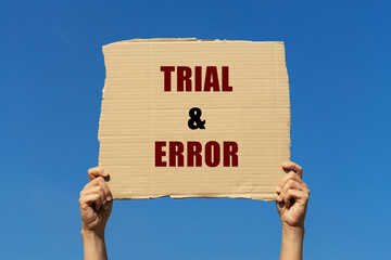 Trial and error text on box paper held by 2 hands with isolated blue sky background. This message board can be used as business concept about trial and error.
