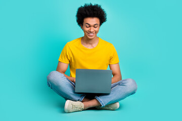 Full length portrait of cheerful nice young man sit floor use wireless netbook isolated on teal color background