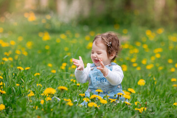 Happy little baby girl sitting on a green meadow with yellow flowers dandelions on the nature in the park