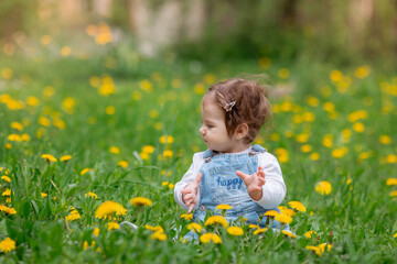 Happy little baby girl sitting on a green meadow with yellow flowers dandelions on the nature in the park