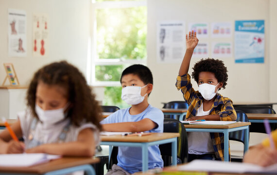 Covid, Students And Education Children In School Classroom Raising Hand To Answer, Ask Or Question Lesson With Classmates. Diverse Group Of Kids, Boys Or Girls With Face Masks Learning In Study Class