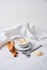 Creamy rice pudding or arroz con leche topped with cinnamon on a white marble background