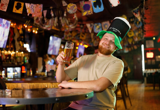 A smiling happy man in a leprechaun hat with beer in pub. He celebrates St. Patrick