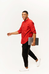 Vertical shot of optimistic handsome man in casual red shirt walking with laptop computer isolated on white background, foreign male student