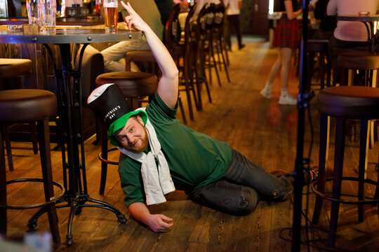 drunk ginger guy in a leprechaun hat for st. patrick's day on the floor orders a beer