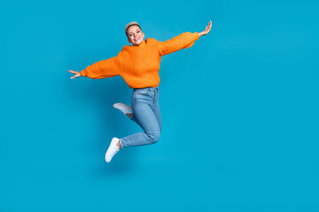 Fototapeta na wymiar Full length photo of carefree shiny dressed knitted pullover jumping high arms sides empty space isolated blue color background