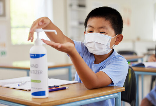 Covid, hand sanitizer and school student with mask cleaning, protecting and staying safe in education classroom. Small, little and cute asian boy in learning in study class preventing spread of virus