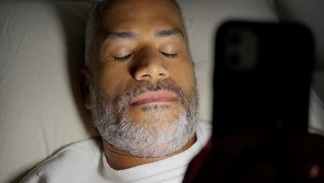 Sleepy black man, falls asleep with mobile phone. Scrolling social media, sleeping problem.