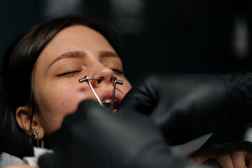 Piercing studio - a master pierces a girl's nose - obrazy, fototapety, plakaty