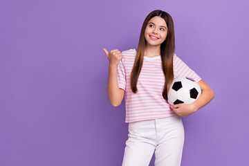 Portrait of charming positive person hold football look indicate finger empty space isolated on purple color background