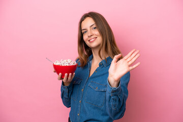 Young caucasian woman holding a bowl of cereals isolated on pink background saluting with hand with...