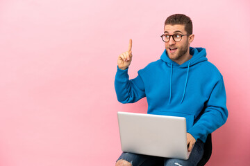 Young man sitting on a chair with laptop intending to realizes the solution while lifting a finger up
