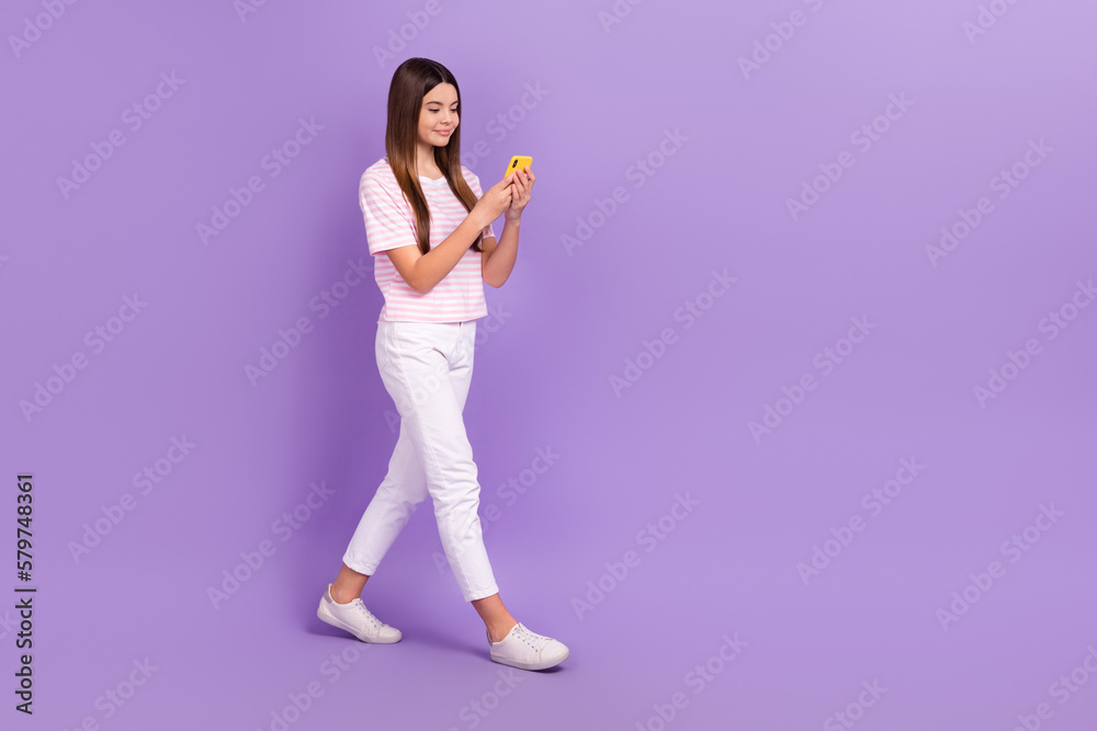 Wall mural Full size profile portrait of charming positive girl walking use telephone empty space isolated on purple color background