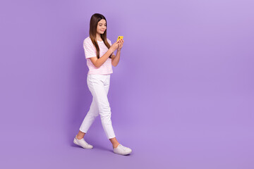 Fototapeta na wymiar Full size profile portrait of charming positive girl walking use telephone empty space isolated on purple color background