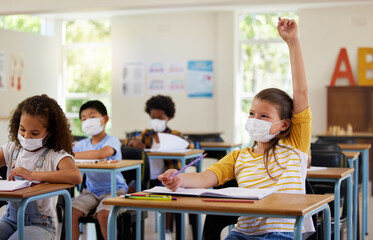 Wearing face mask to protect from covid while learning in class, answering education question and studying with students in a classroom. Girl sitting at a desk and raising hand during a pandemic