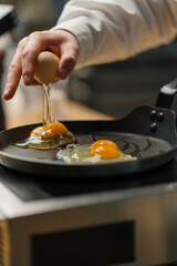 A cook breaks an egg into a pan Preparing breakfast in a professional kitchen
