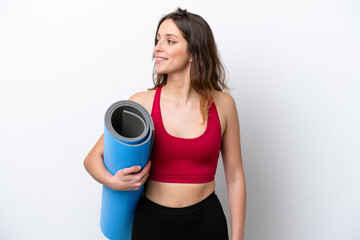 Young sport caucasian woman going to yoga classes while holding a mat isolated on white background looking side