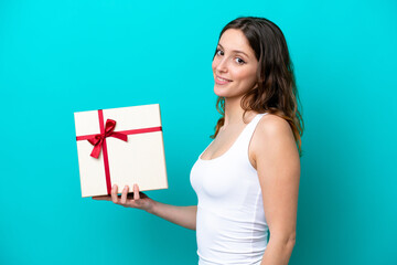 Young caucasian woman holding a gift isolated on blue background smiling a lot
