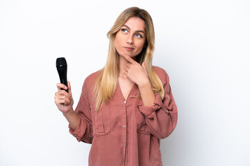 Singer Uruguayan woman picking up a microphone isolated on white background having doubts