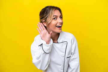 Uruguayan chef woman isolated on yellow background listening to something by putting hand on the ear