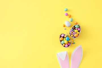 Easter celebration idea. Top view photo of easter bunny ears chocolate eggs with сolorful dragees and sprinkles on isolated yellow background with copyspace