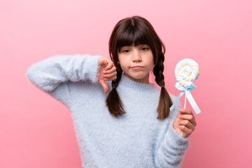 Little caucasian girl holding a lollipop showing thumb down with negative expression