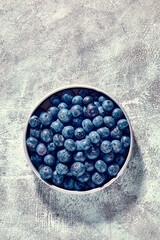 Top down shot of fresh blueberries picked into dish standing on grey texture table background.